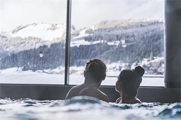 Couple qui admire la vue du village enneigé depuis le bassin du spa Océane - L.Meyer - Châtel