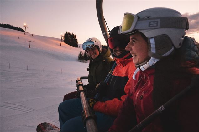 Un groupe de skieurs sur en télésiège à la tombée de la nuit avant de rejoindre les pistes du domain